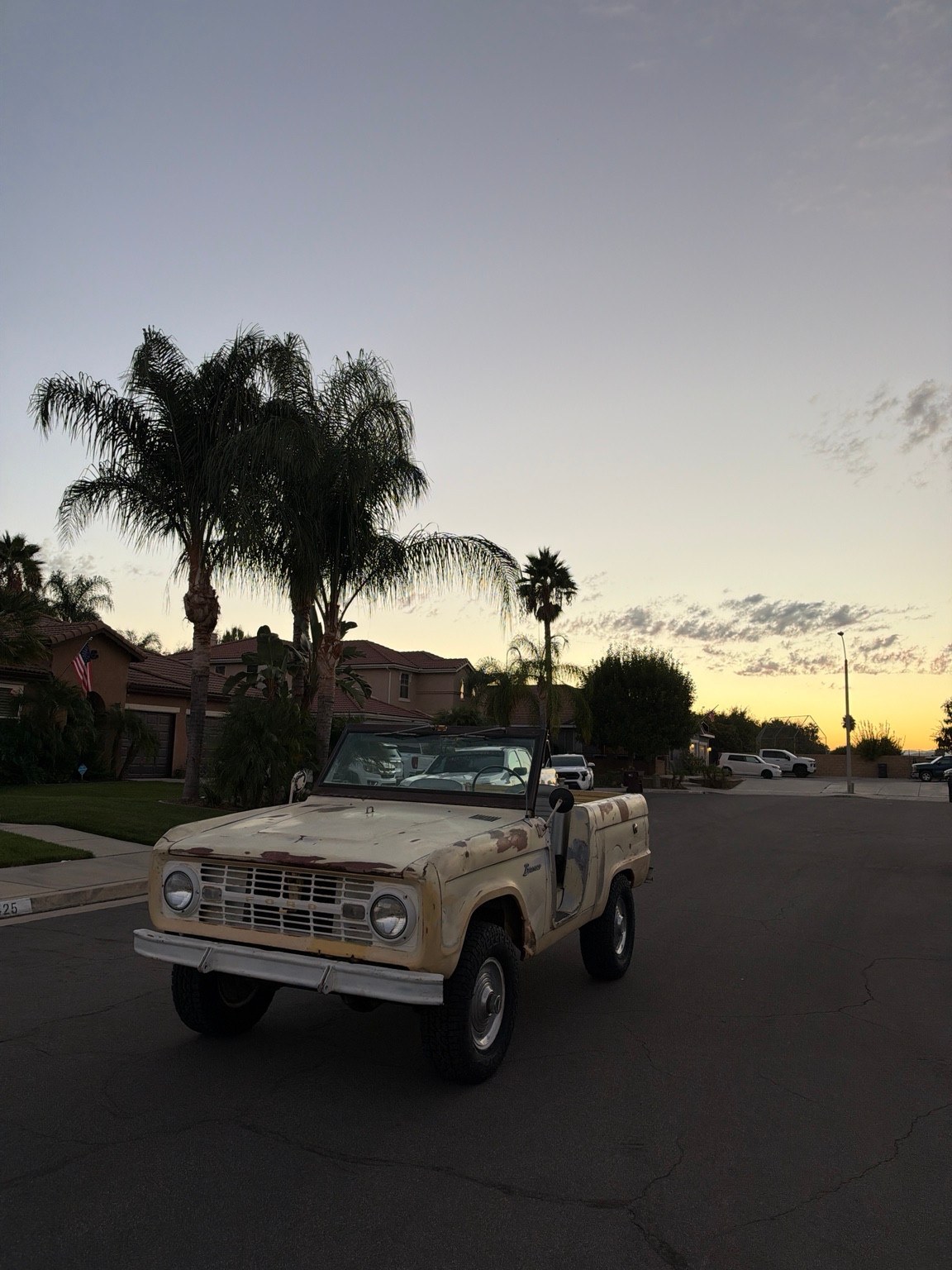 Front three-quarter view of the weathered pale yellow 1966 Bronco U13 beneath a sunset sky.