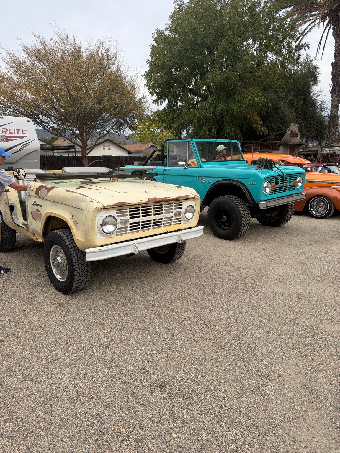 The pale yellow Bronco U13 survivor parked beside a turquoise Bronco and other classic vehicles.